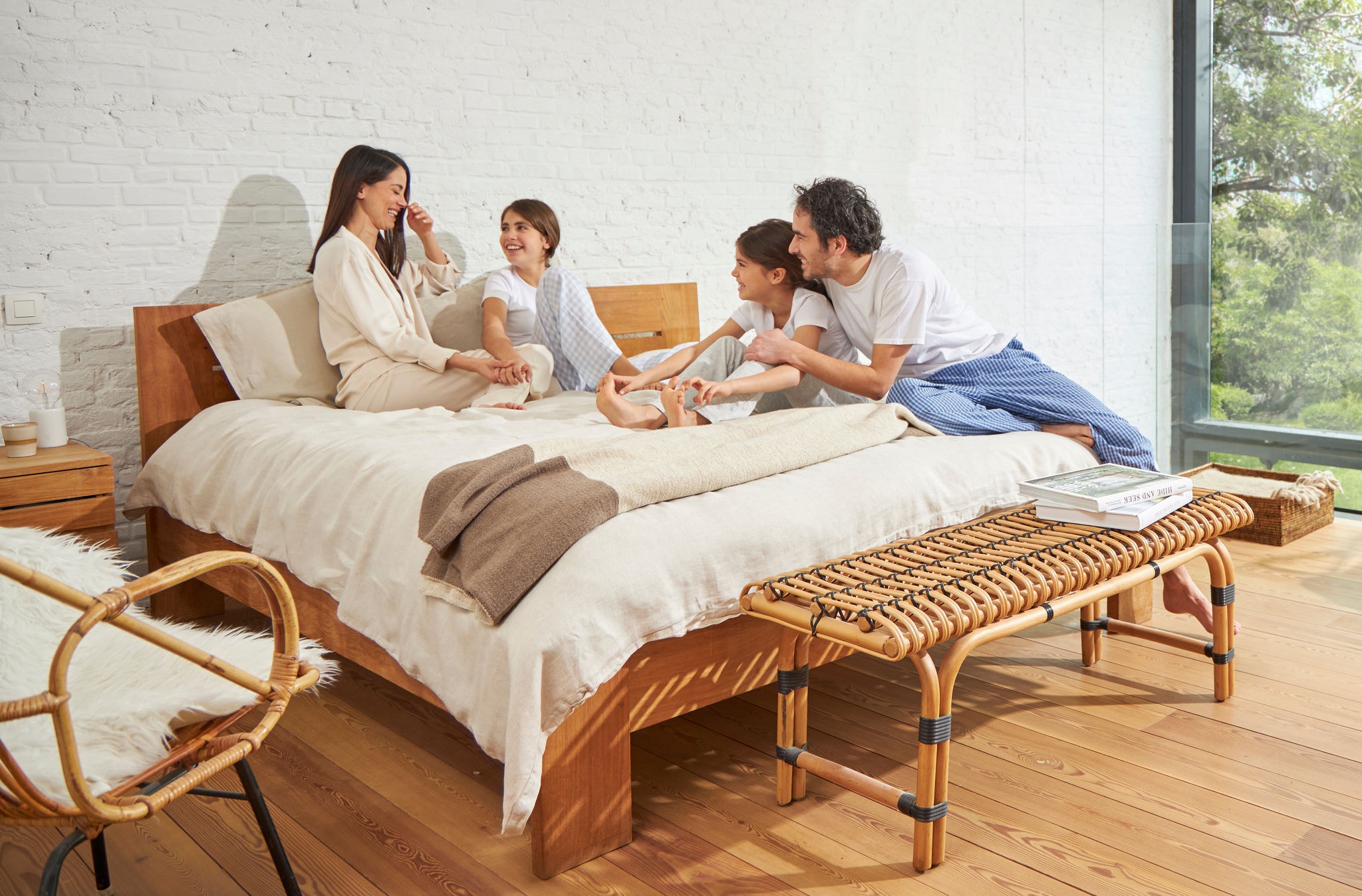 Kobieta i mężczyzna siedzący na łóżku z dwiema młodymi dziewczynkami, zrelaksowani, roześmiani i cieszący się zdrowym powietrzem.