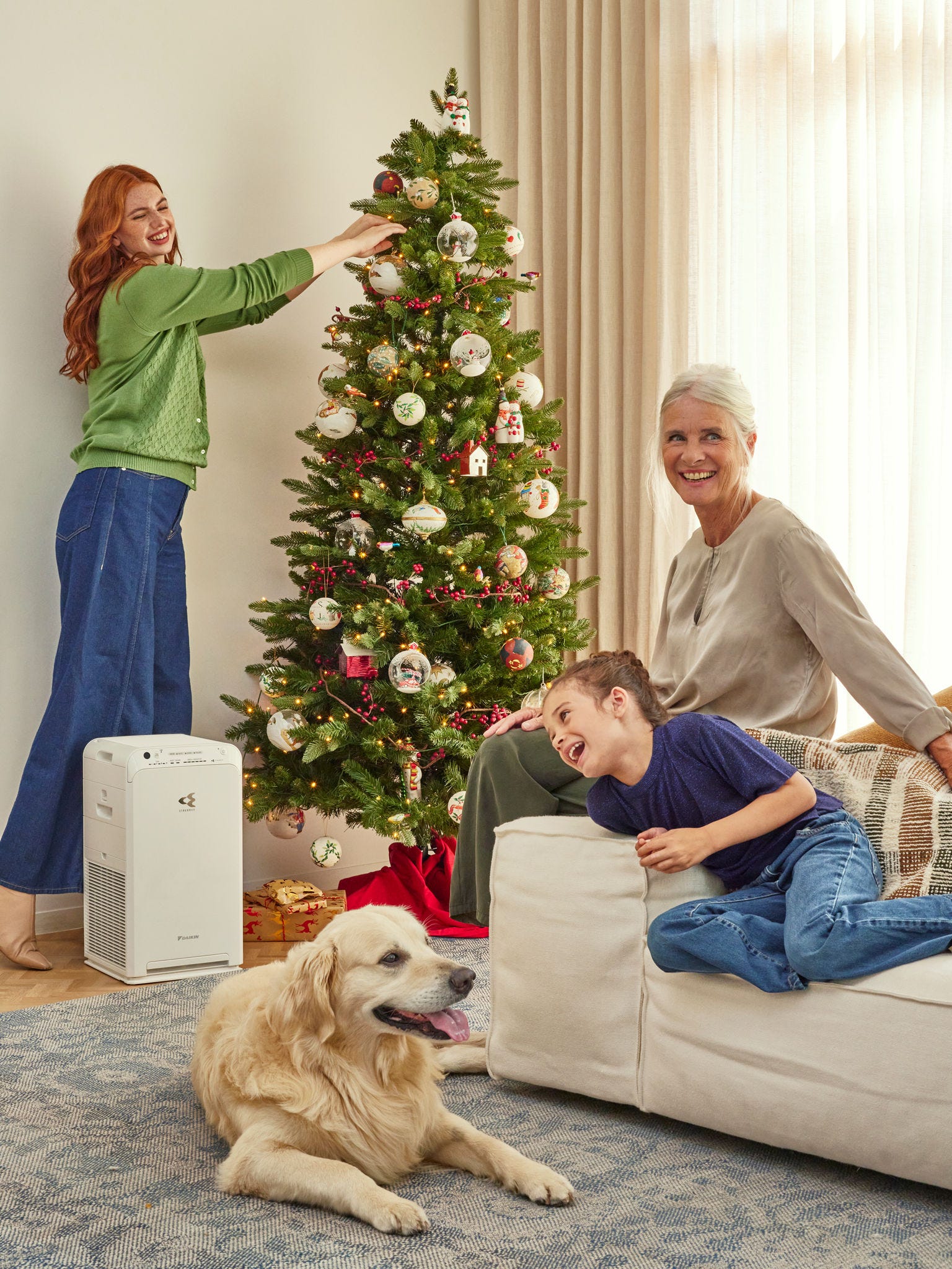 Kobieta i dziecko siedzą na kanapie, śmiejąc się. W tle widoczna jest świąteczna choinka oraz oczyszczacz powietrza Daikin