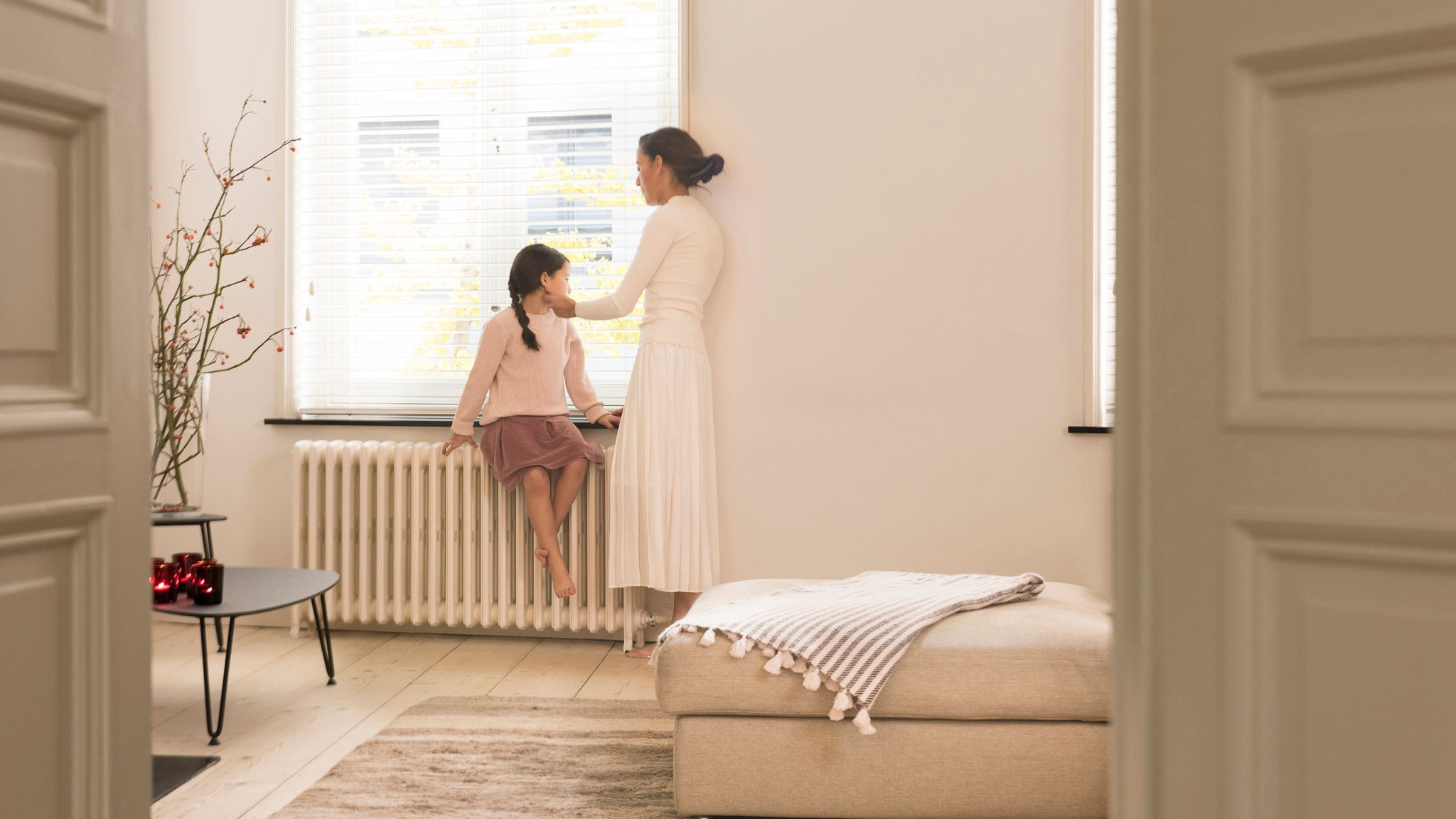 Mama i córka rozmawiają i ogrzewają się przy grzejniku.