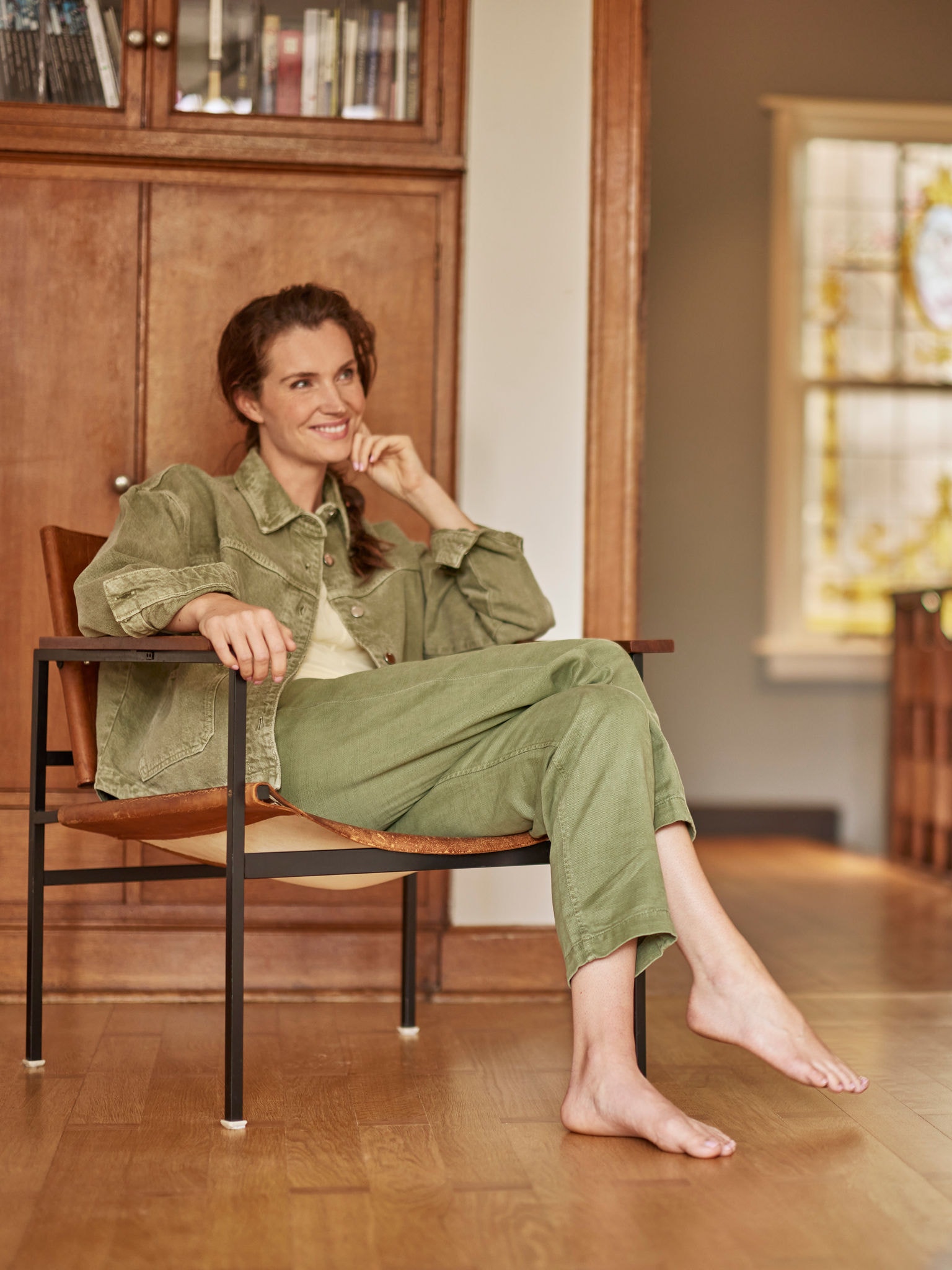 Kobieta siedząca w fotelu, boso, uśmiecha się i patrzy przed siebie