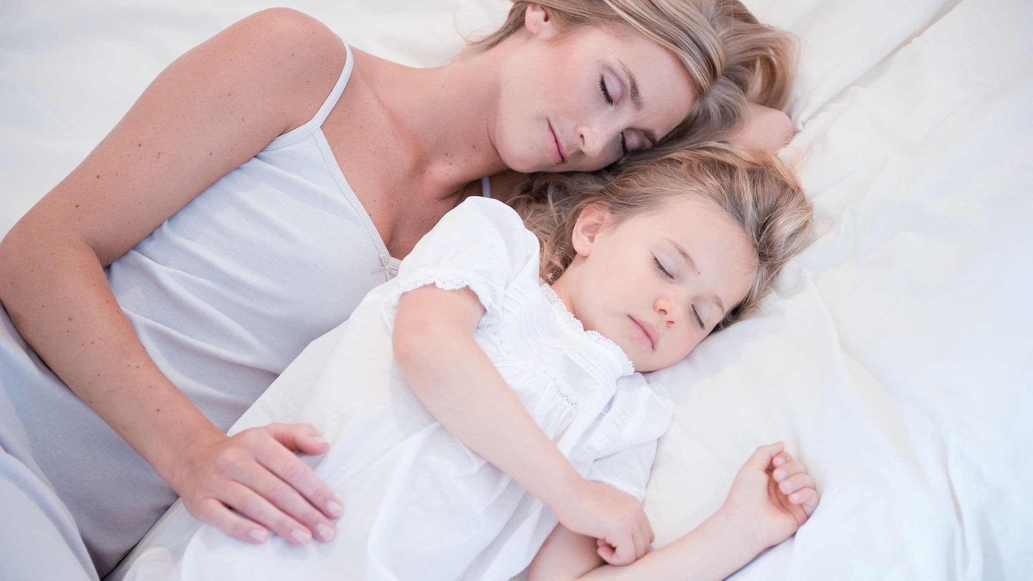 Mama i córeczka śpiące obok siebie w białym łóżeczku w czystym powietrzu.