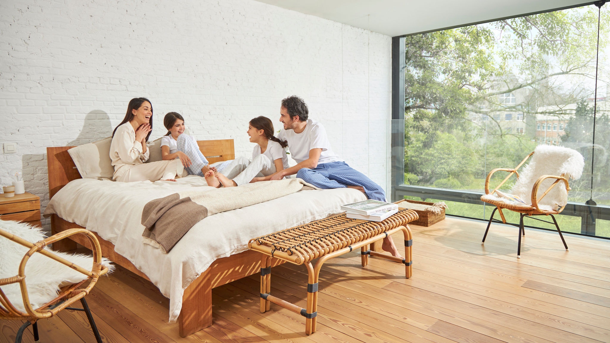 Rodzina rozmawia na łóżku w sypialni z dużą szklaną ścianą, gdzie jakość powietrza w pomieszczeniu jest dobra, a światła naturalnego jest pod dostatkiem