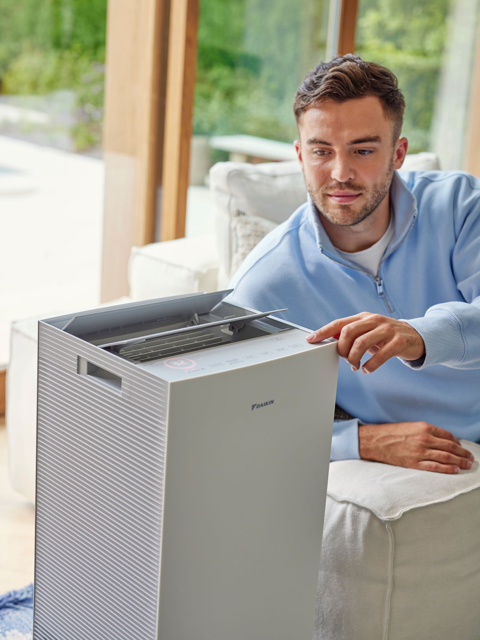 Mężczyzna reguluje oczyszczacz powietrza Daikin w salonie, aby ograniczyć obecność alergenów kocich