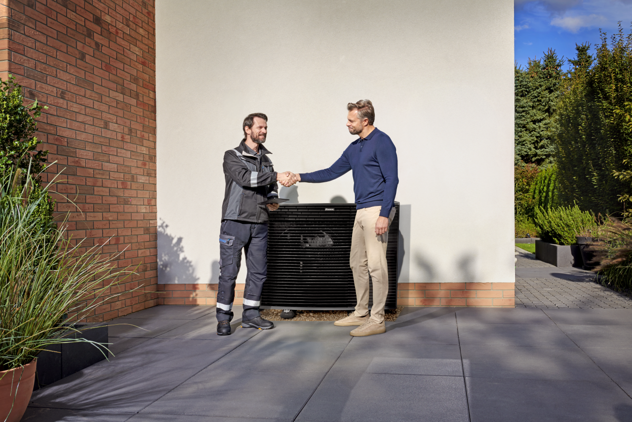 Instalator ściskający dłoń klienta przed jednostką zewnętrzną Daikin Altherma